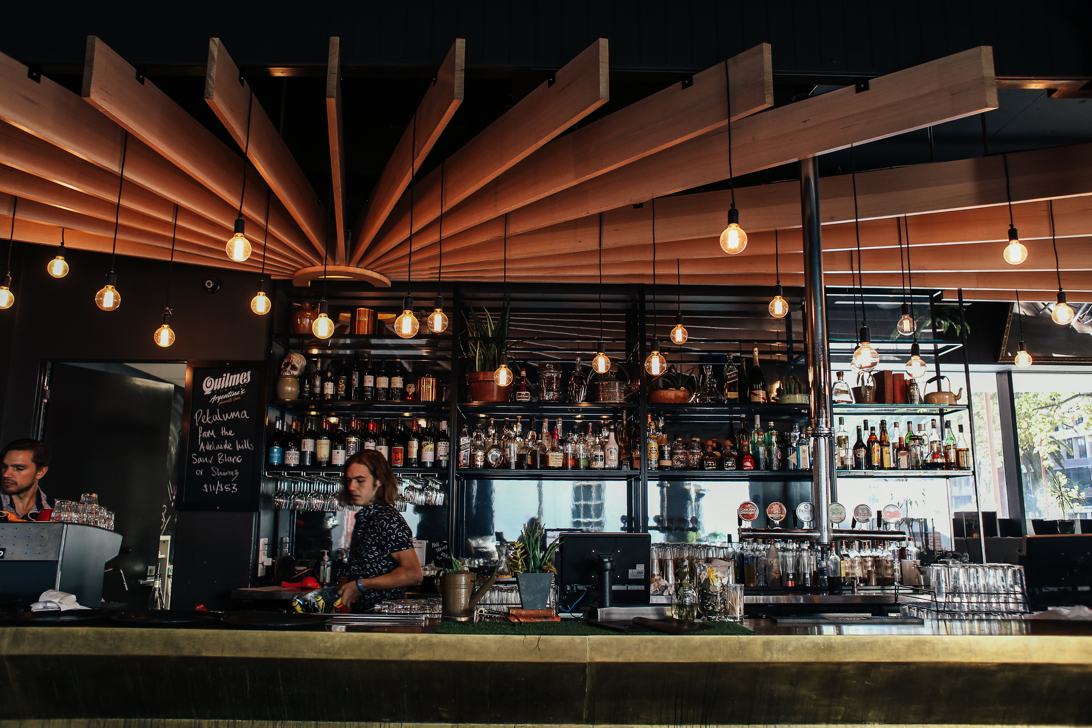 Shelves, Beams and Lights over Men behind a Bar